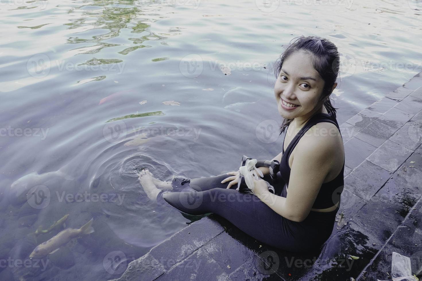 attraente giovane donna seduta di il bordo di un' nuoto piscina, Tenere un' Google foto