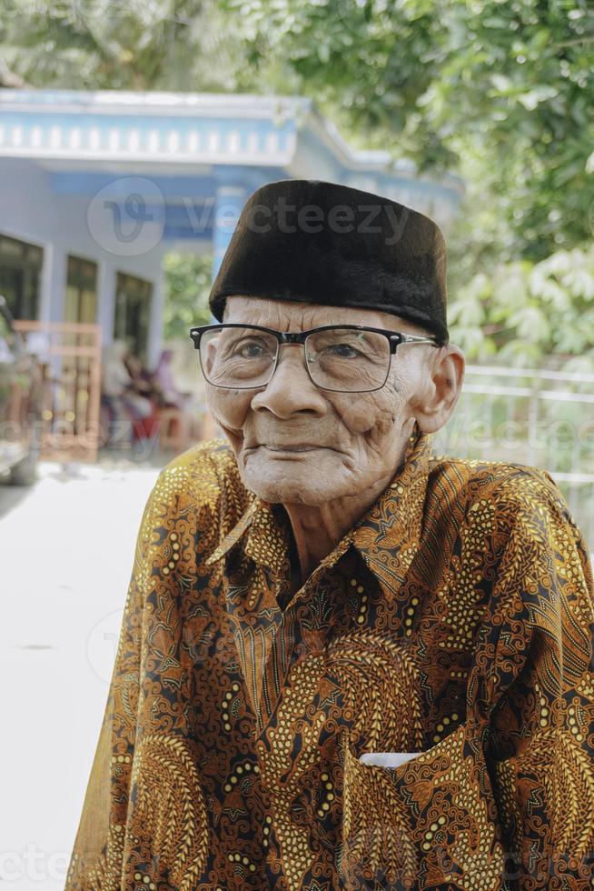 un' ritratto di un vecchio asiatico uomo indossare batik camicia e bicchieri foto