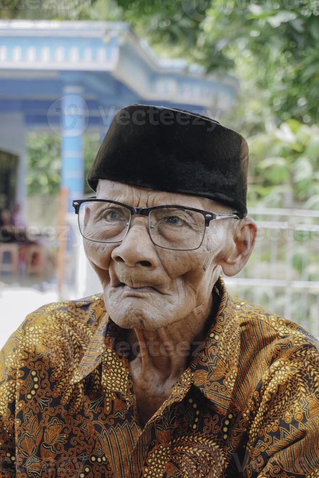 un' ritratto di un vecchio asiatico uomo indossare batik camicia e bicchieri foto