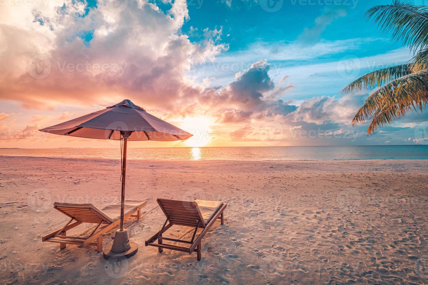 bellissimo scenario del tramonto tropicale, due lettini, lettini, ombrellone sotto la palma. sabbia bianca, vista mare con orizzonte, cielo crepuscolare colorato, calma e relax. hotel ispiratore del resort sulla spiaggia foto