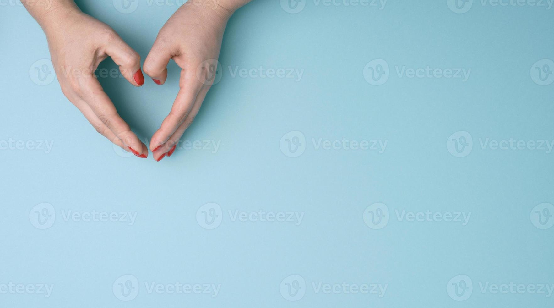 Due femmina mani piegato nel il forma di un' cuore su un' blu sfondo. foto