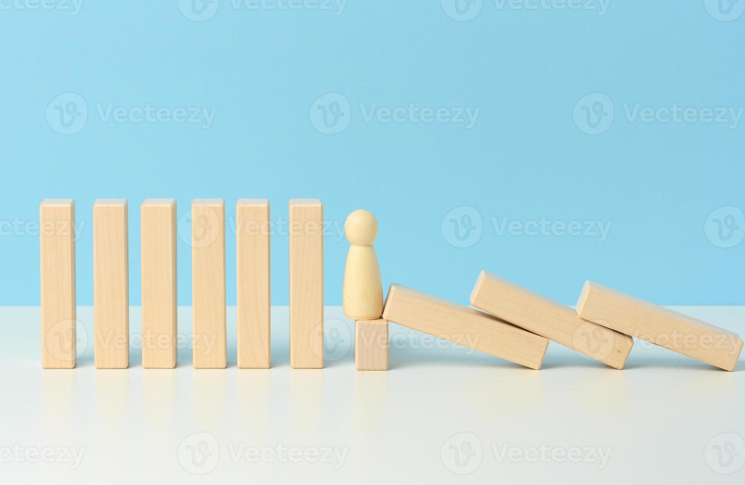 figure di uomini trattenere il caduta di di legno blocchi, il effetto di domino su un' blu sfondo. concetto di lavoro di squadra foto