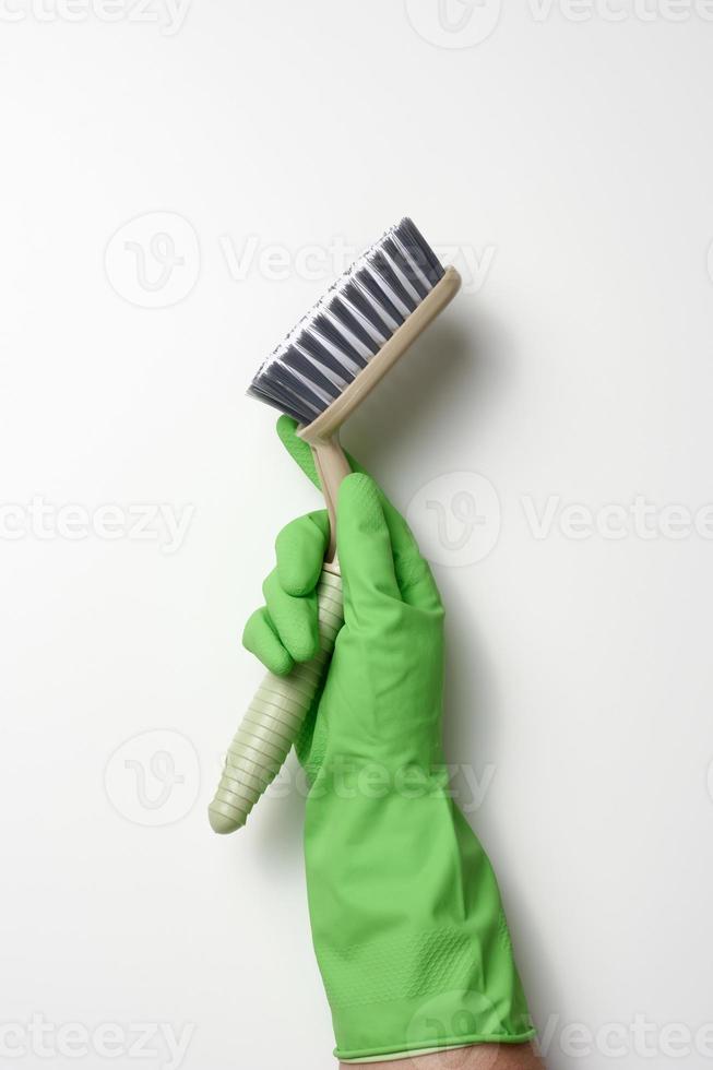 mano nel un' verde gomma da cancellare pulizia guanto detiene un' plastica spazzola su un' bianca sfondo foto