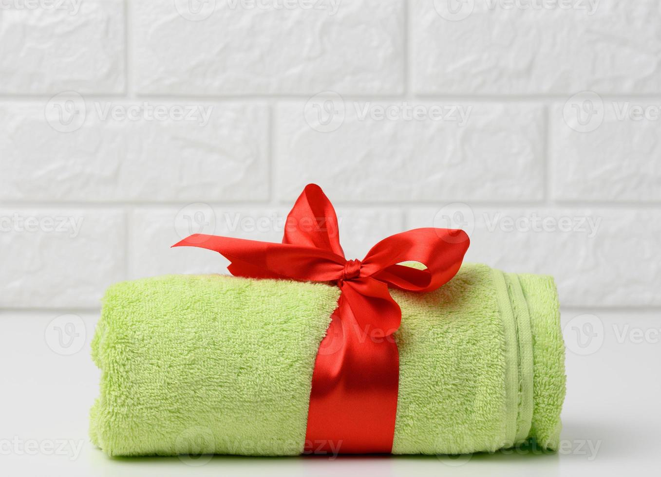 lanciato su spugna verde asciugamano legato con rosso seta nastro su bianca mensola nel bagno foto