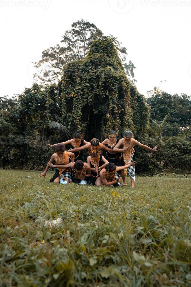 un' gruppo di indonesiano persone danza posa nel un' d'oro completo da uomo mentre indossare trucco su il verde erba foto