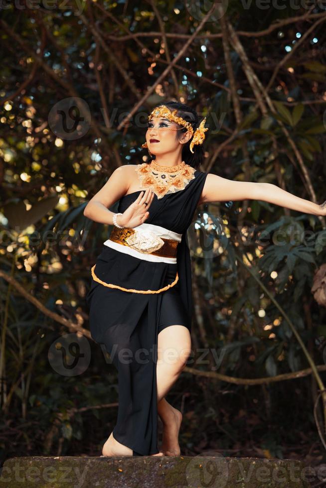 balinese donna danza su il superiore di il roccia mentre indossare un' nero costume e un' d'oro corona su sua testa foto