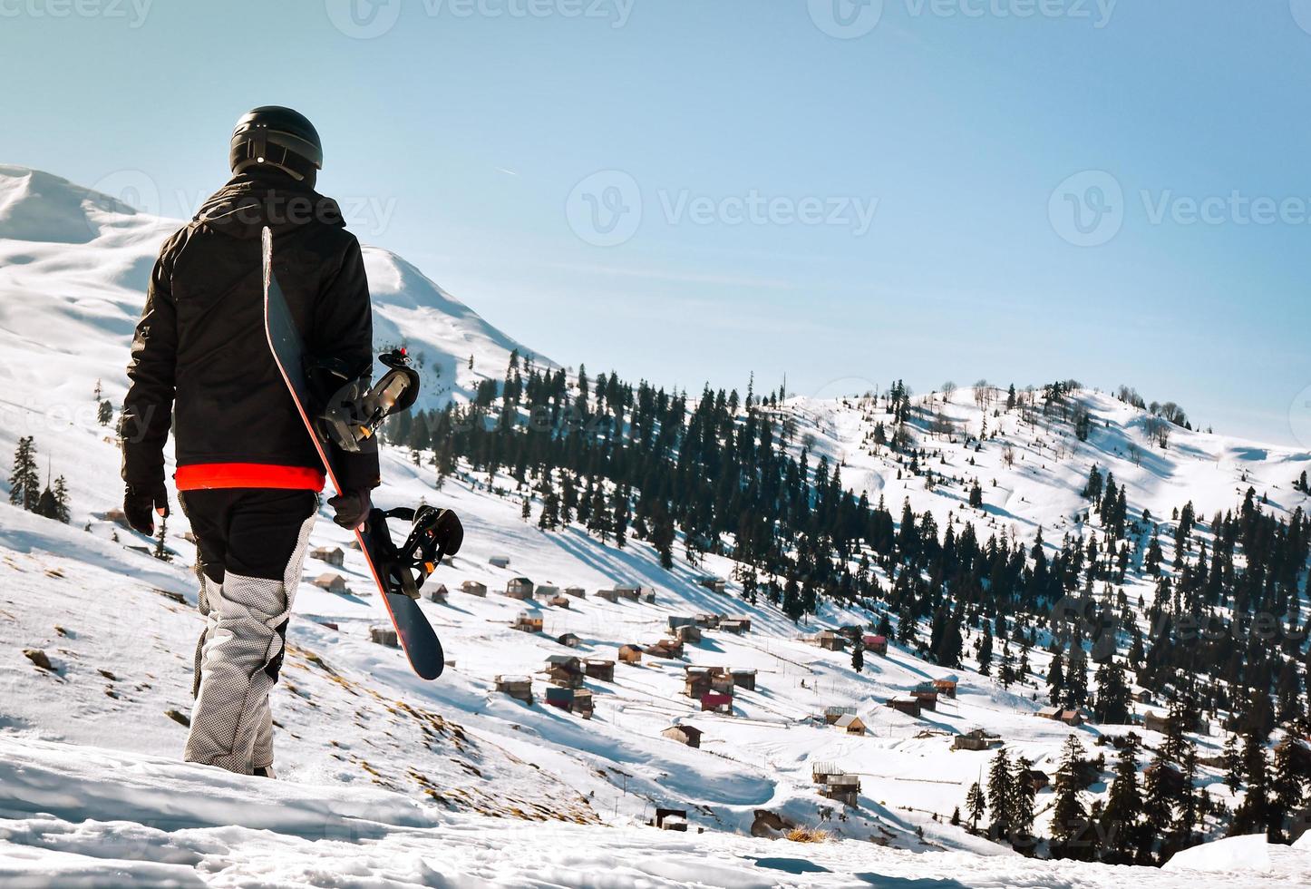 uomo turista nel sciare completo da uomo con Snowboard nel il suo mani passeggiate a innevato pendenza contro il fondale di bellissimo montagna paesaggio foto