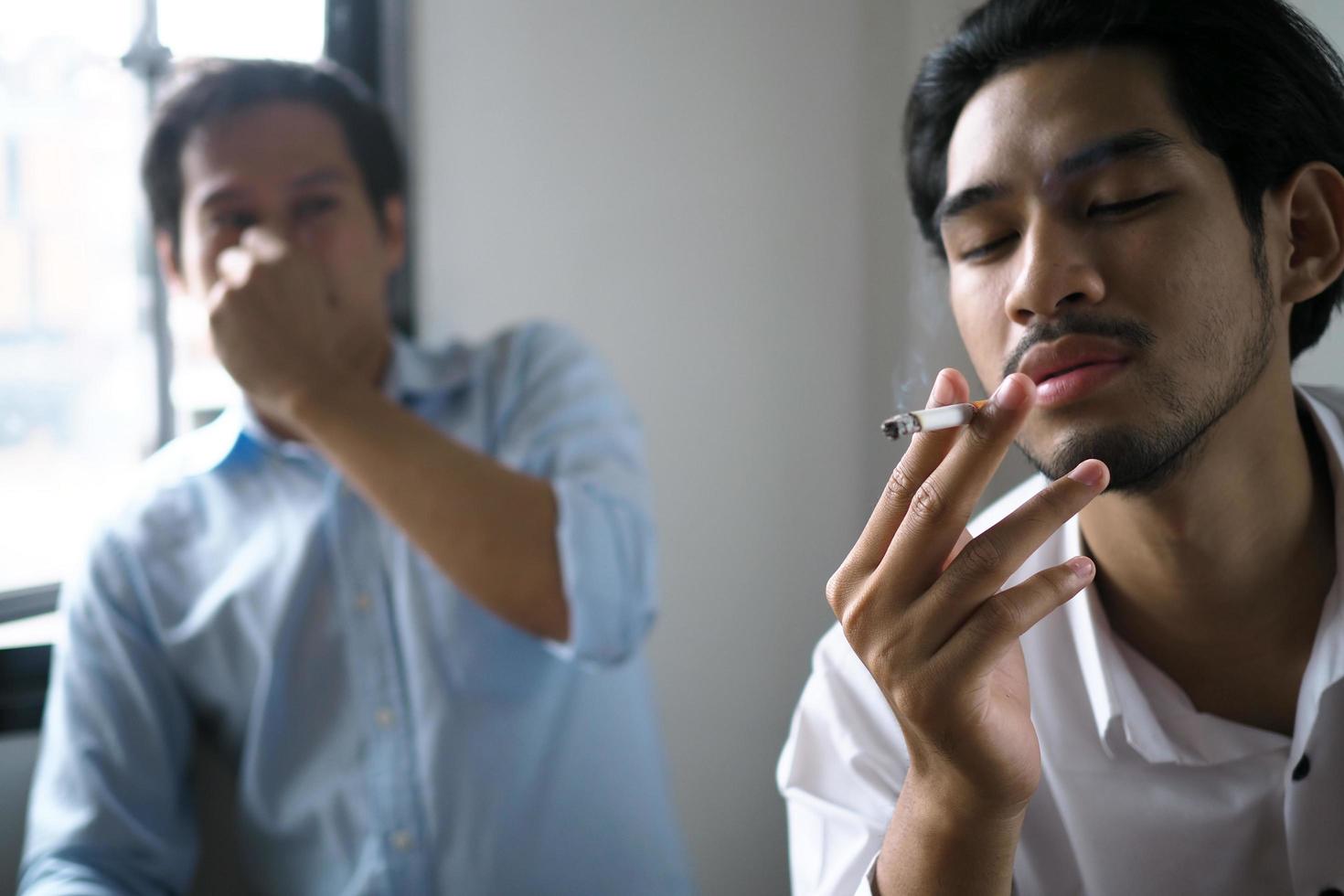 uomo siamo fumo nel il ufficio. colleghi annusato sigarette e espresso disgusto. foto