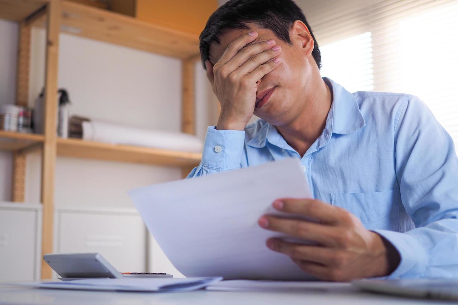 un' attività commerciale persona seduta nel il testa stressato con debito conto di reddito e spese quello siamo tenuto nel mano. foto