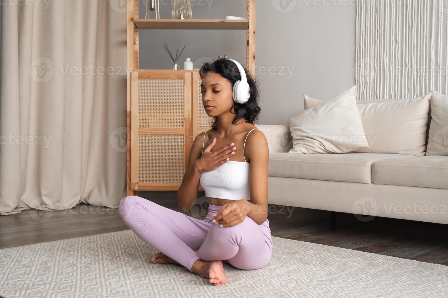 lato Visualizza su giovane in forma salutare africano americano donna nel abbigliamento sportivo seduta a casa fare yoga, Meditare e respirazione nel il mattina. mentale Salute e benessere concetto foto