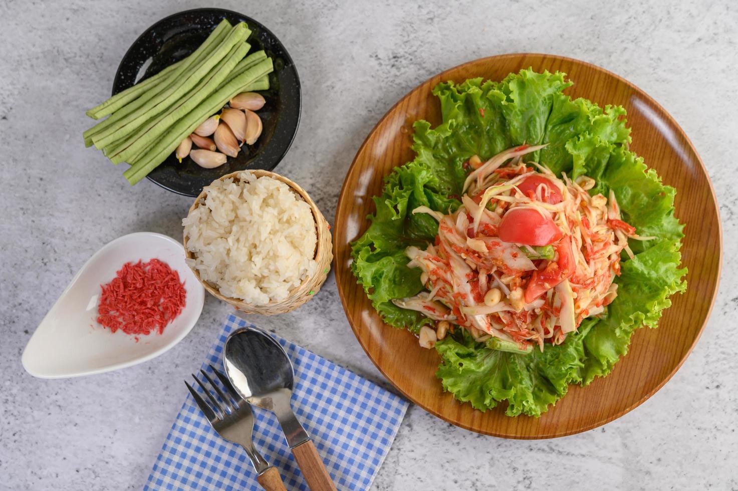 insalata di papaya tailandese con riso appiccicoso, cucchiaio e forchetta foto