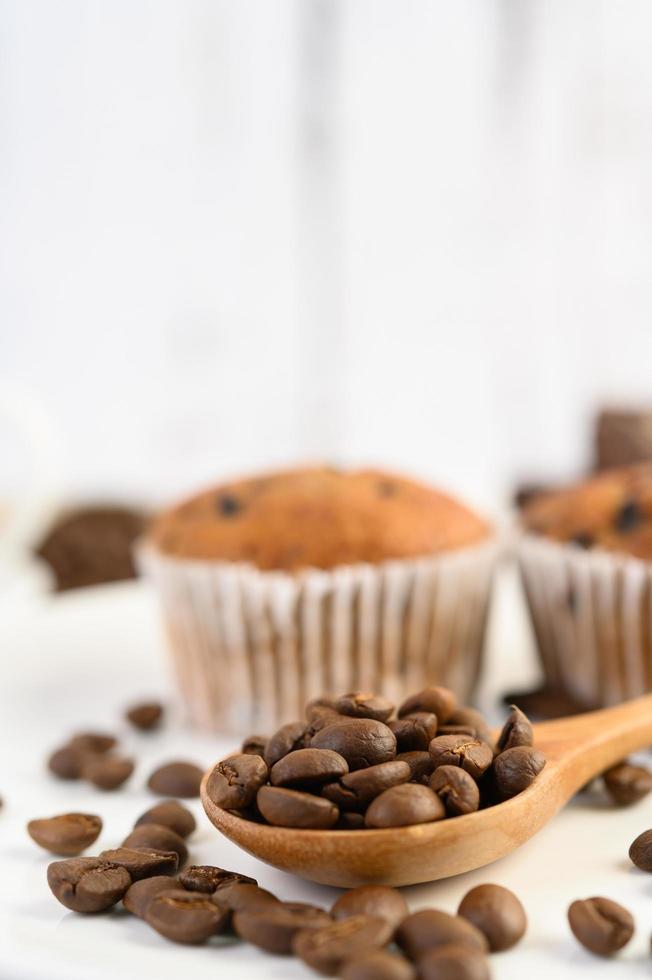 chicchi di caffè su un cucchiaio di legno e cupcakes alla banana su un tavolo di legno bianco foto