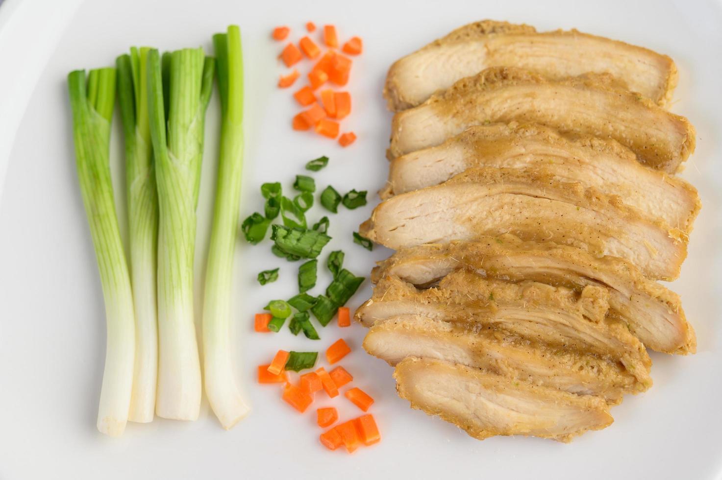 petto di pollo al vapore su un piatto bianco con cipolline e carote foto