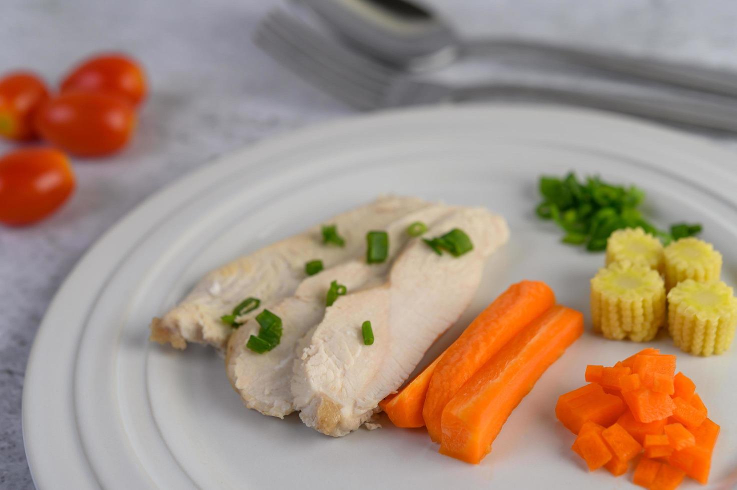 petto di pollo al vapore su un piatto bianco con cipolline, mais baby e carote foto