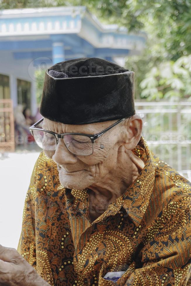 un' ritratto di un vecchio asiatico uomo indossare batik camicia e bicchieri foto