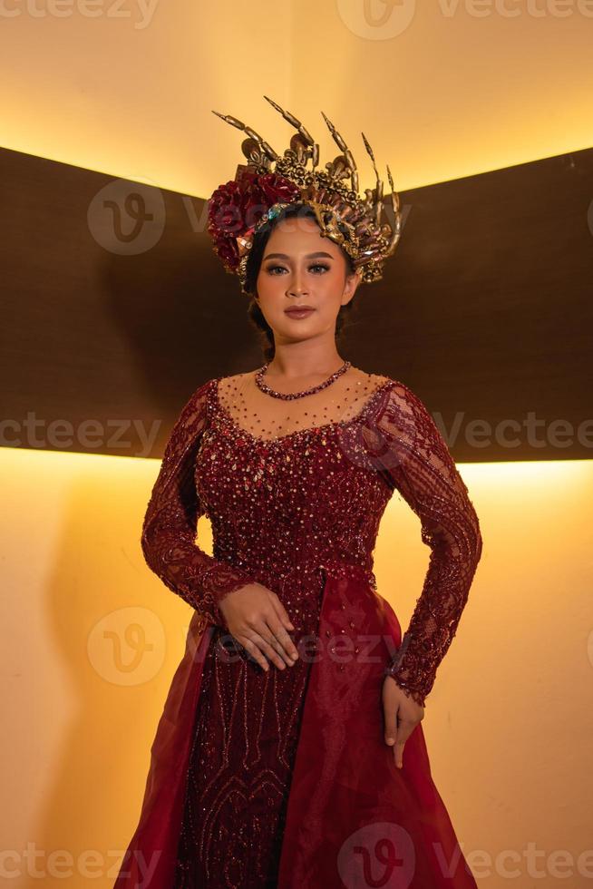 asiatico donna nel rosso vestito in posa con un' oro corona su sua testa foto