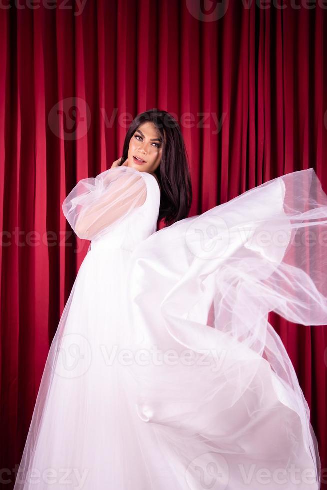 bellissimo asiatico donna in posa nel un' volante nozze vestito nel davanti di il rosso tenda foto