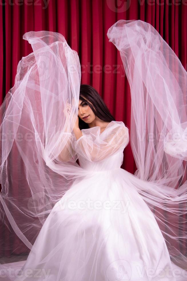 eleganza asiatico donna indossare un' nozze vestito con volante tessuto in giro sua nel davanti di il rosso tenda foto