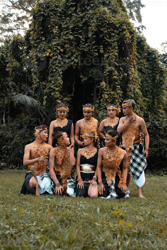 un' gruppo di indonesiano persone danza posa nel un' d'oro completo da uomo mentre indossare trucco su il verde erba foto