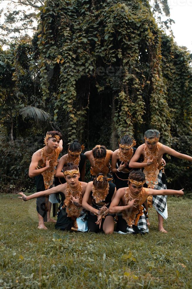 un' gruppo di indonesiano persone danza posa nel un' d'oro completo da uomo mentre indossare trucco su il verde erba foto