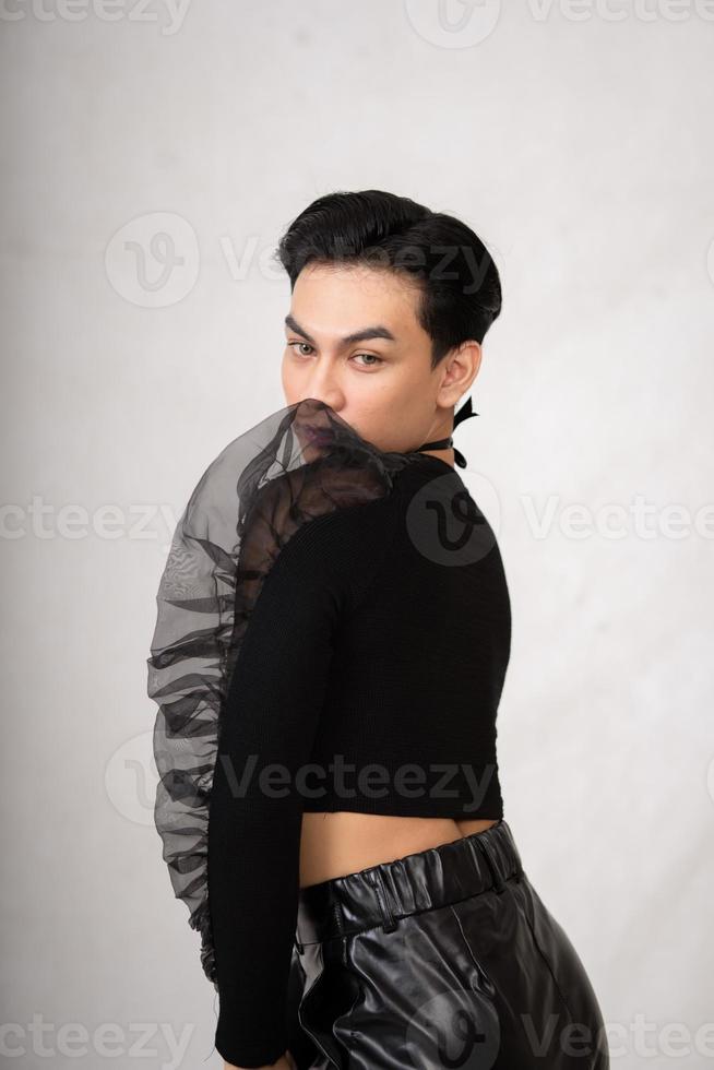 un' transgender uomo pose nel un' nero vestito con un eleganza viso e nero capelli foto