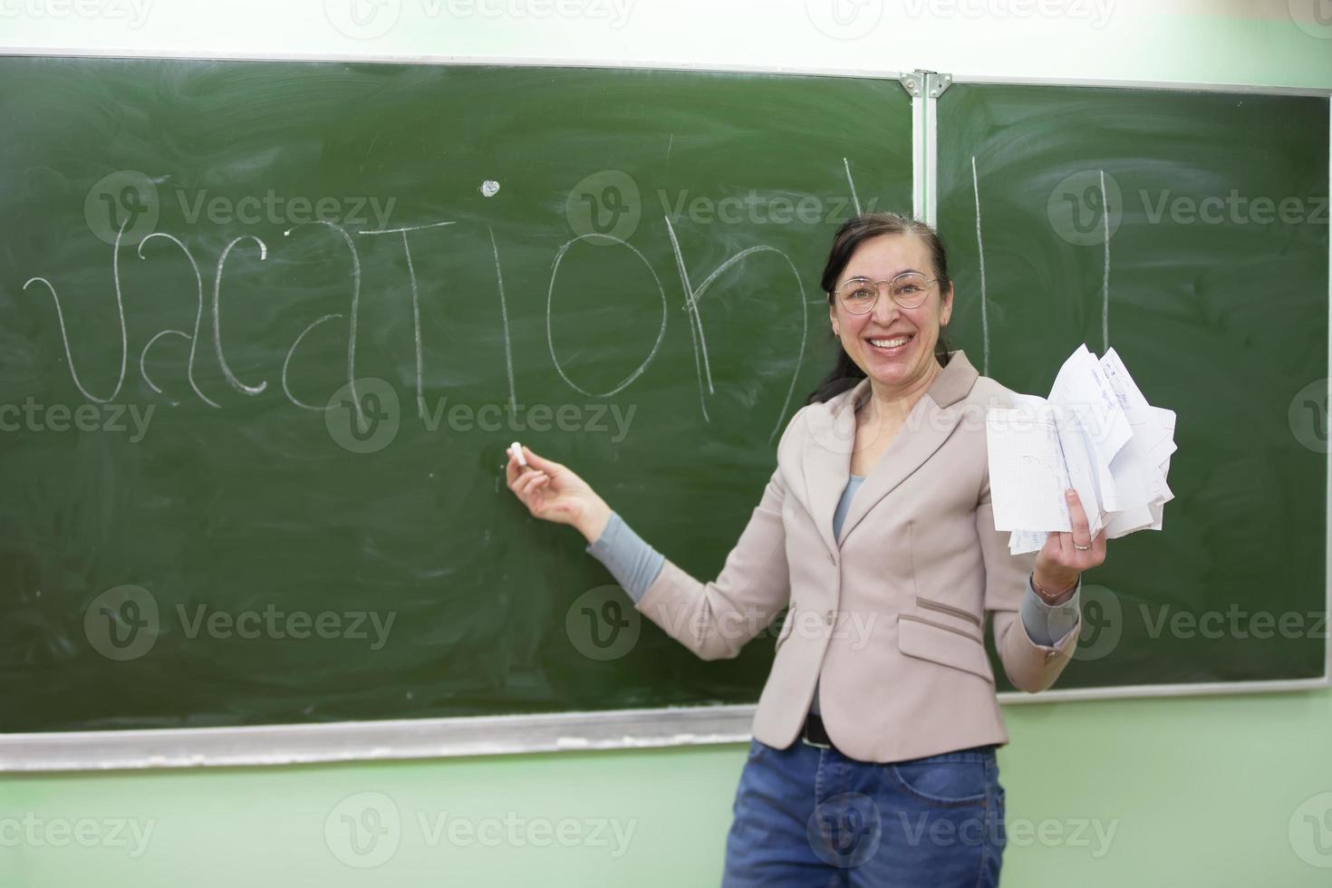 contento insegnante scrive il parola vacanza su il lavagna. foto