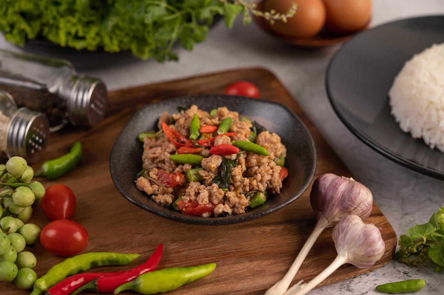 insalata di maiale macinata piccante con riso, peperoncino e pomodori su un piatto nero foto