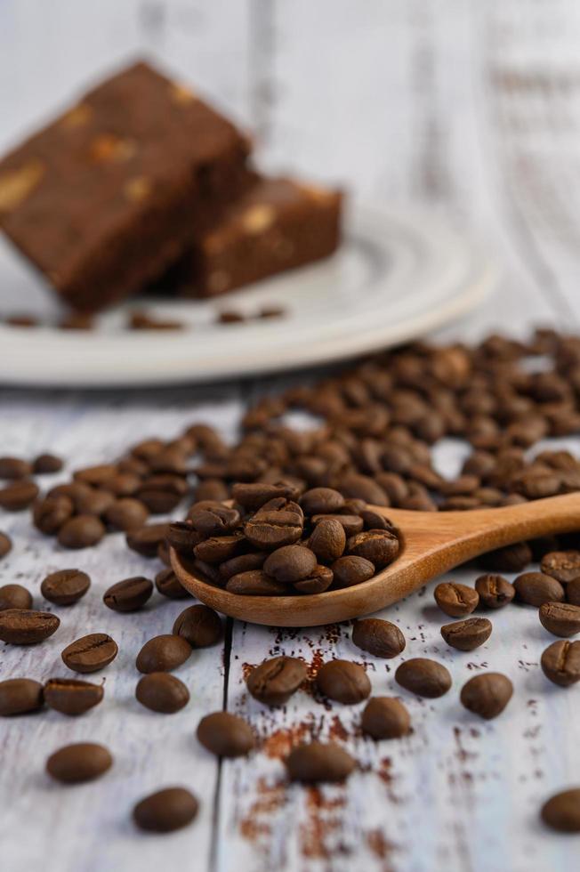 chicchi di caffè sul cucchiaio di legno e brownie al cioccolato su un tavolo di legno bianco foto