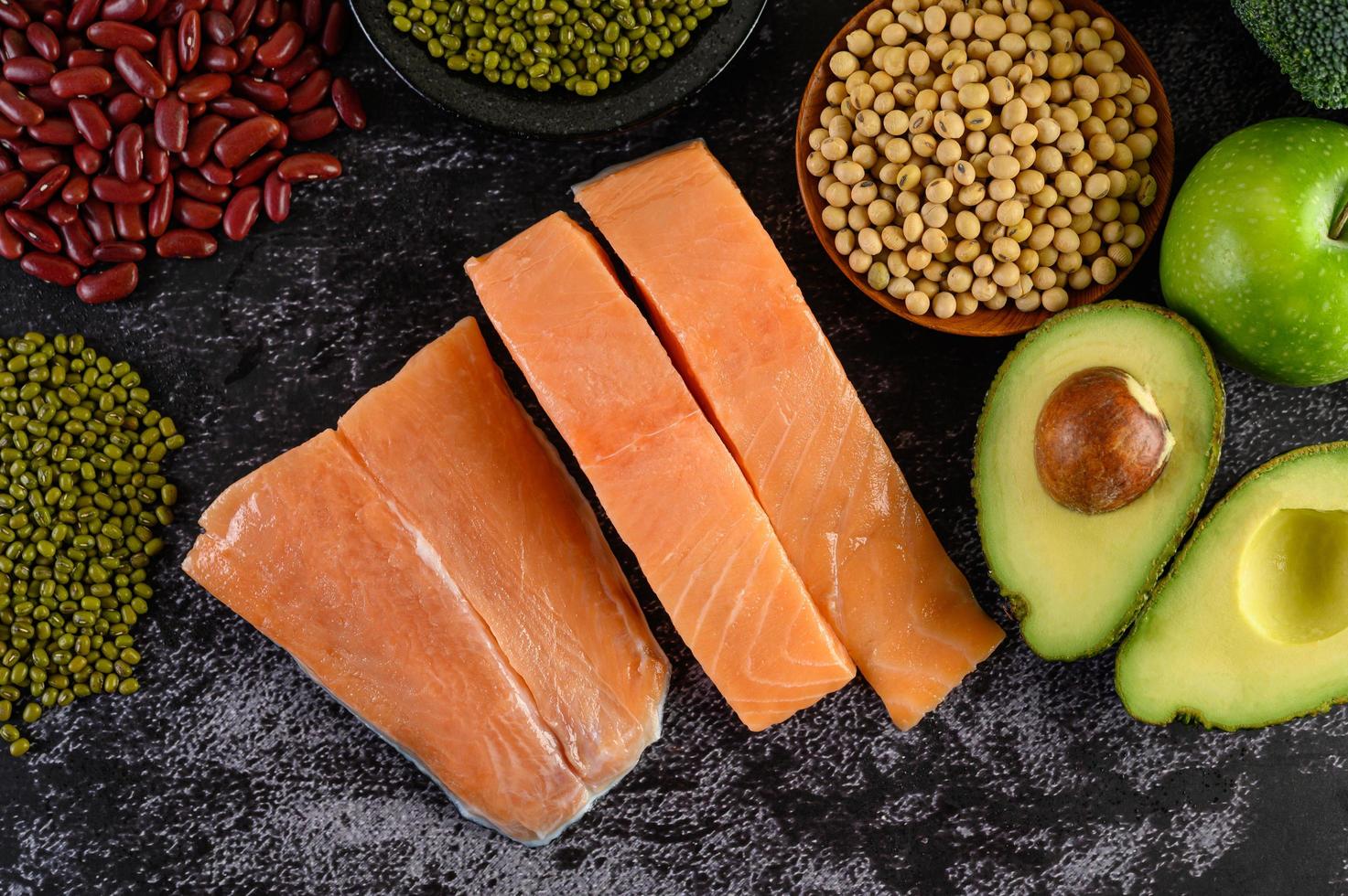 legumi, frutta e salmone su uno sfondo di cemento nero foto