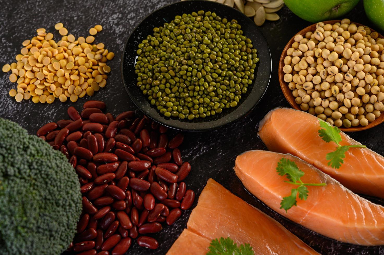 legumi, broccoli, frutta e salmone su uno sfondo di cemento nero foto