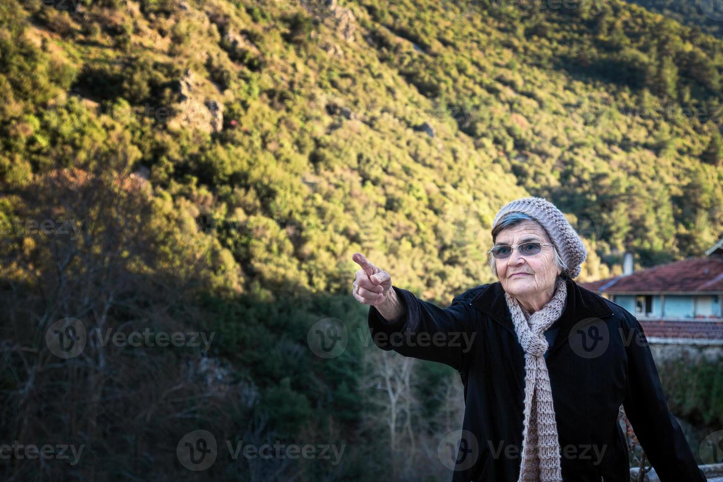 anziano donna nel nero giacca e cappello puntamento a il montagne foto