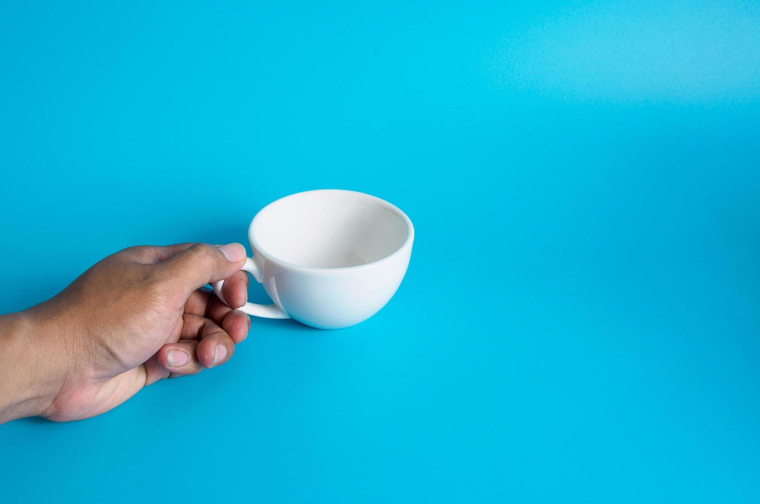 uomo mano Tenere un' bianca caffè tazza, pieno con caldo nero caffè Americano, no zucchero no latte, pronto per bere, rinfrescante. aroma sveglio fresco per opera posto su un' blu isolato sfondo foto