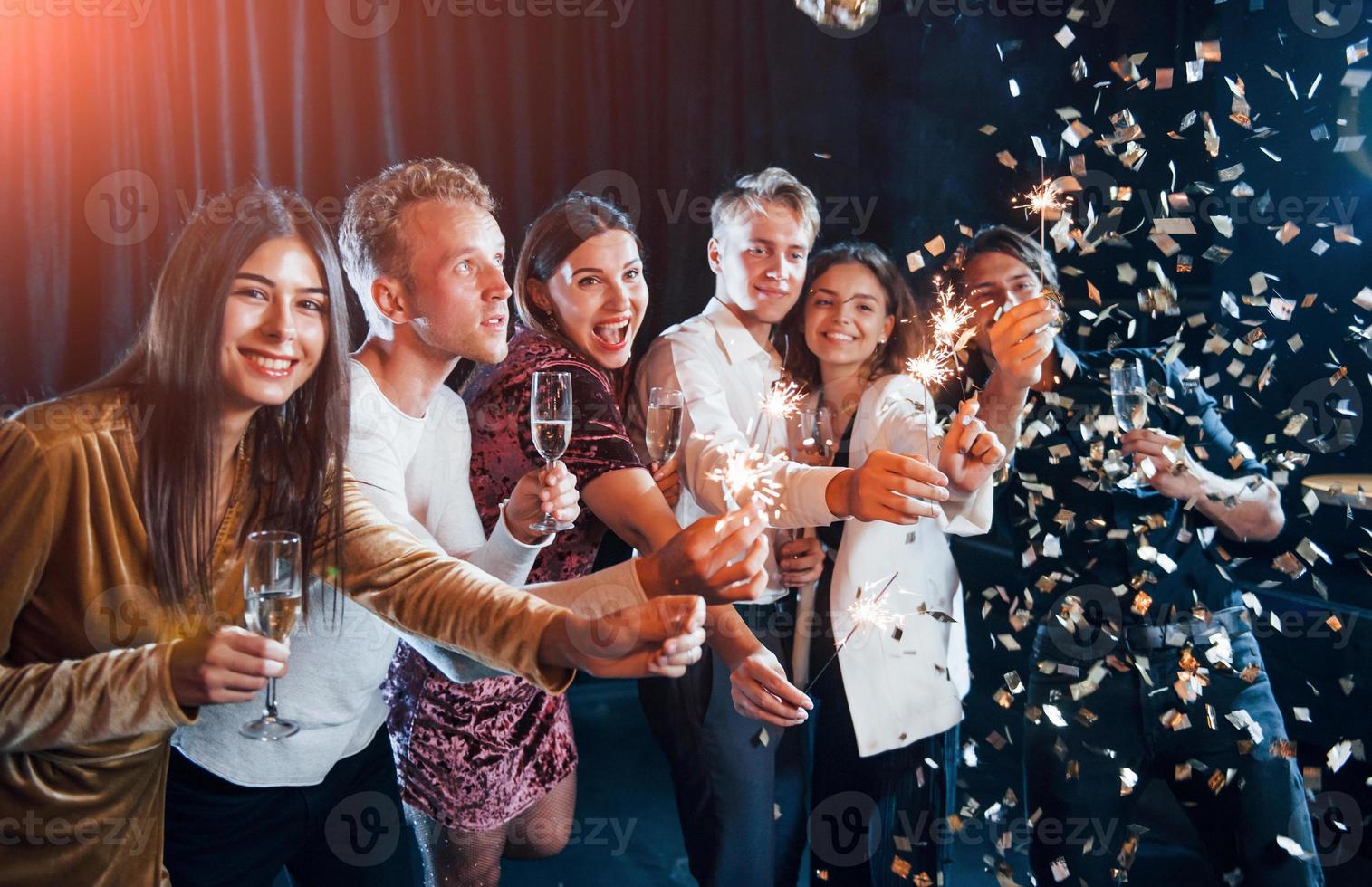 avendo divertimento con spumanti. coriandoli è nel il aria. gruppo di allegro amici festeggiare nuovo anno in casa con bevande nel mani foto