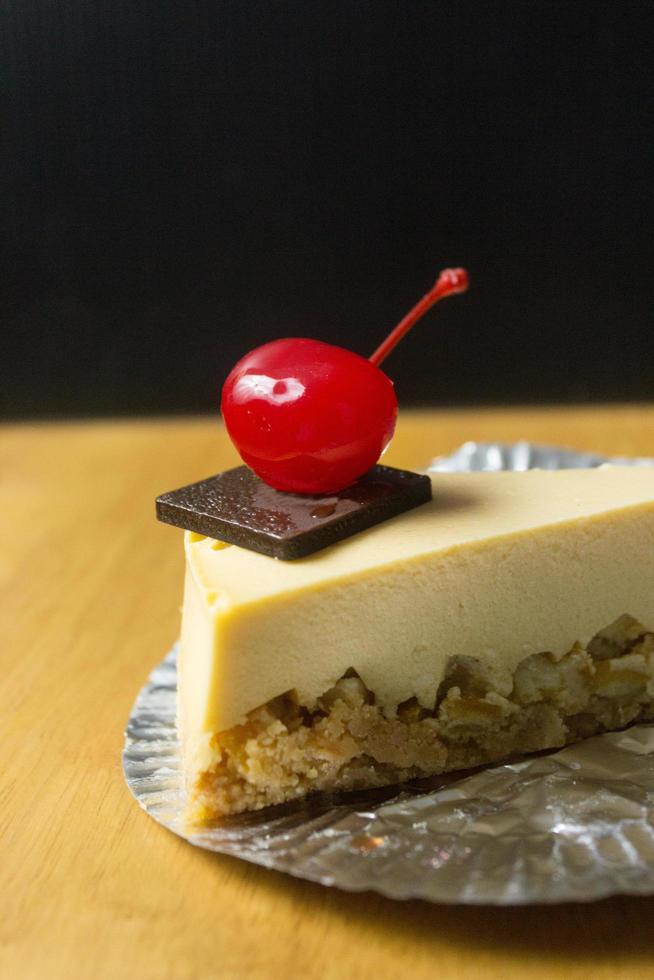 fetta di torta di formaggio con cioccolato e ciliegia sul tavolo di legno foto