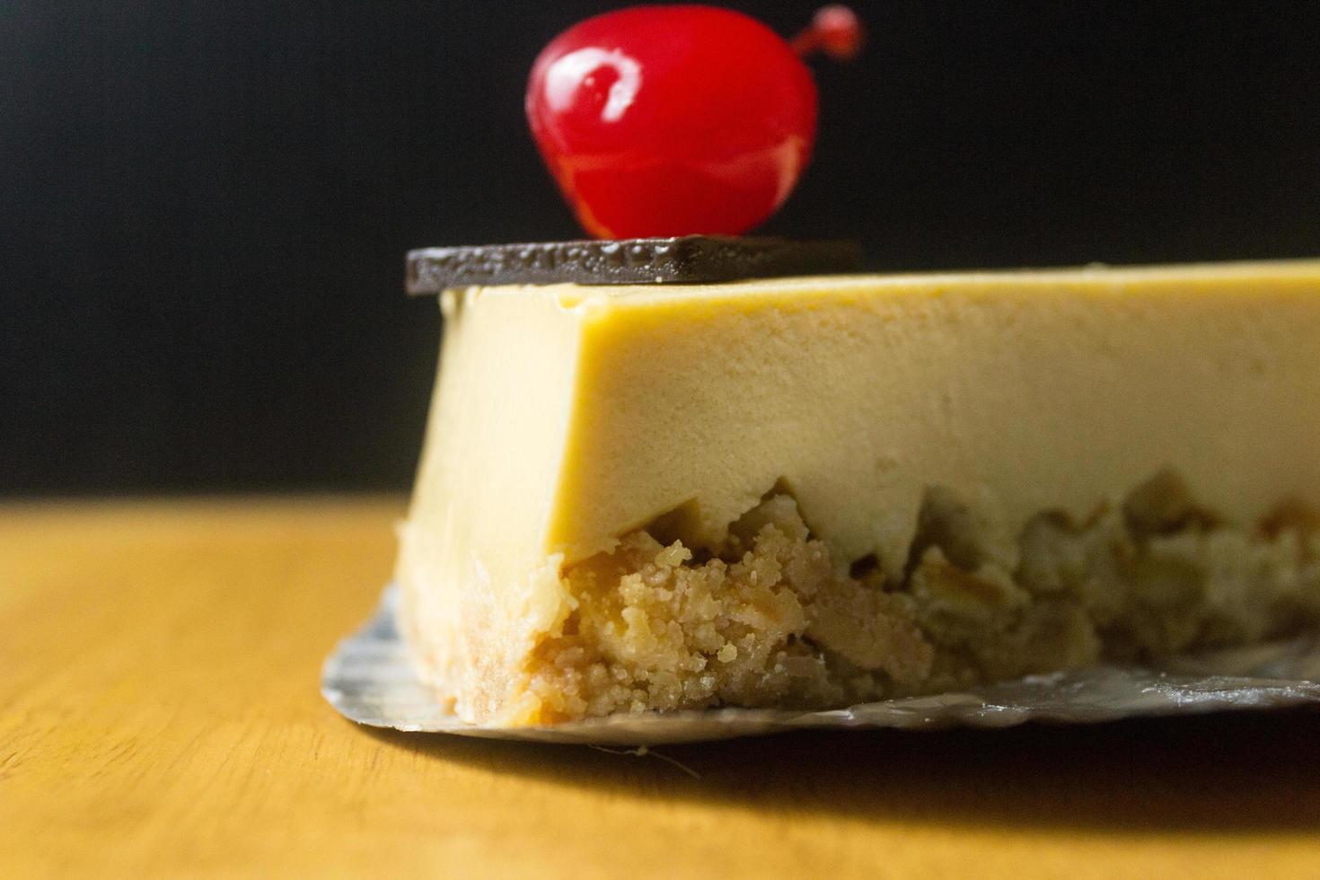 fetta di torta di formaggio con cioccolato e ciliegia sul tavolo di legno foto