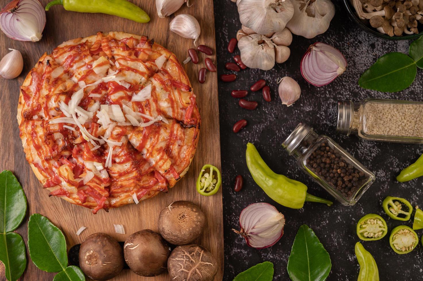 pizza su una tavola di legno con peperoni, aglio, peperoncino e funghi shiitake foto