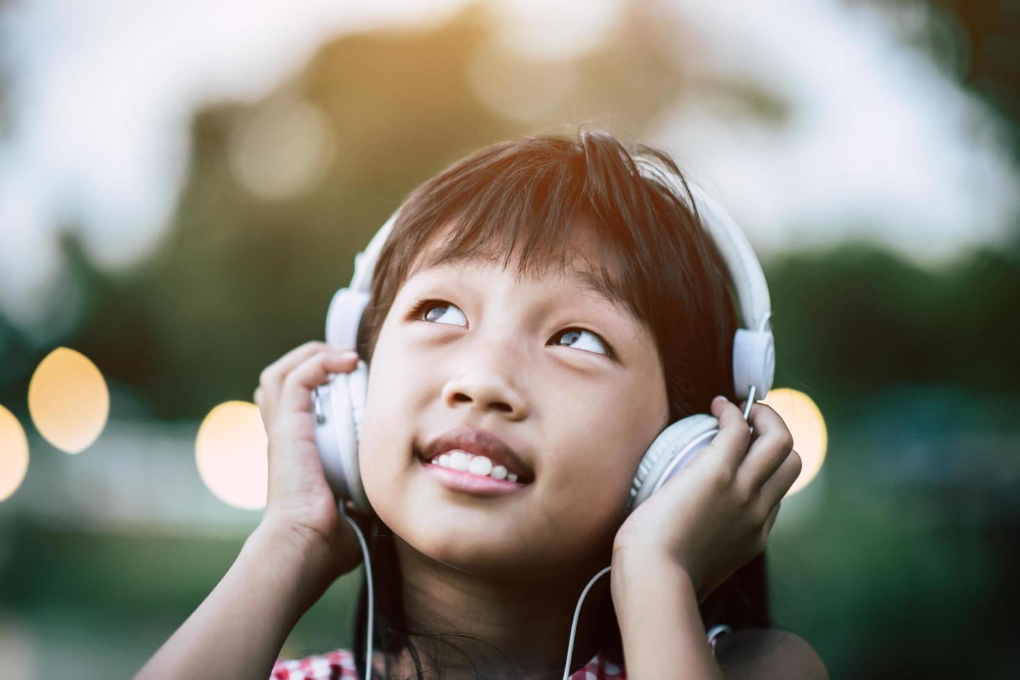 bambina che ascolta la musica nel parco con le cuffie foto