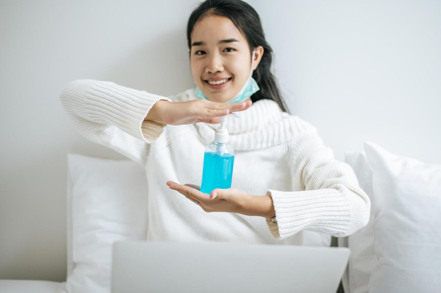 giovane donna sul letto tenendo il gel per il lavaggio delle mani foto