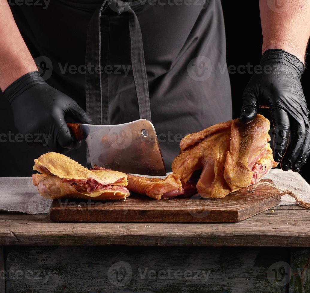 capocuoco nel nero uniforme e latice guanti chopping crudo pollo in pezzi foto