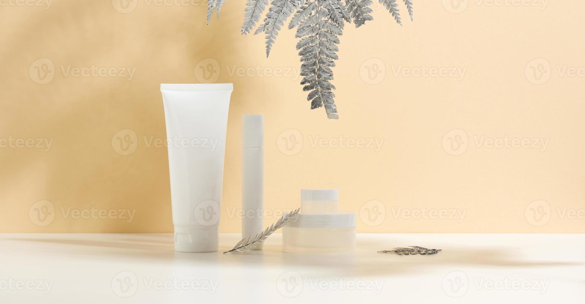bianca tubo per cosmetici, un' vaso di crema e argento foglia su un' bianca tavolo. cosmetico su un' beige ombra sfondo. crema bottiglia, lozione, detersivo, shampoo per cura della pelle foto