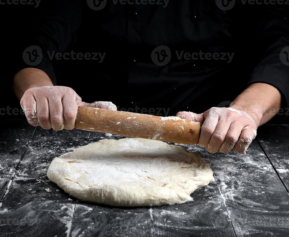 capocuoco nel un' nero tunica rotoli un' Impasto per un' il giro Pizza foto