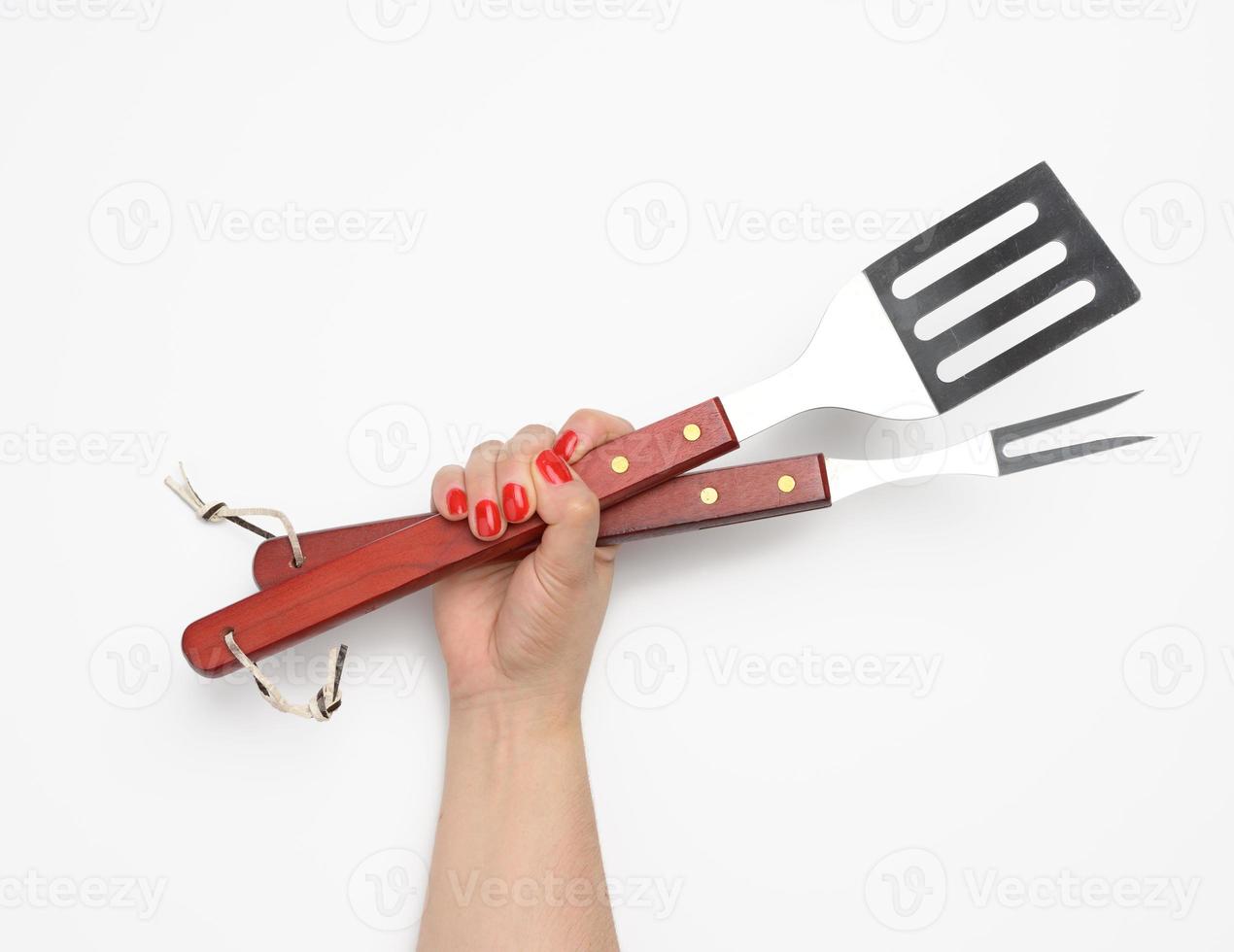 metallo spatola e forchetta con un' di legno maniglia per un' picnic nel un' femmina mano con dipinto rosso Chiodi su un' bianca sfondo foto