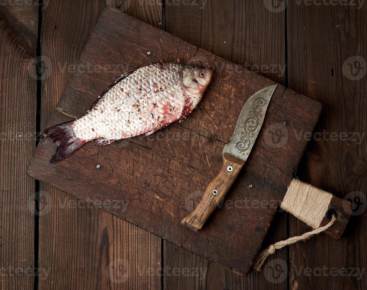 fresco carassio pesce cosparso con spezie bugie su un' Marrone di legno taglio tavola foto