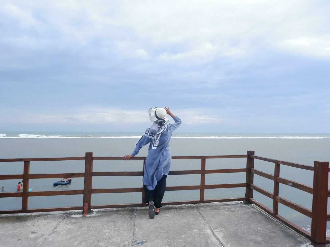 indietro di il donna nel il cappello su il tropicale spiaggia chi era guardare a il cielo e il mare mentre diffusione sua mani su il ponte. mare Visualizza foto