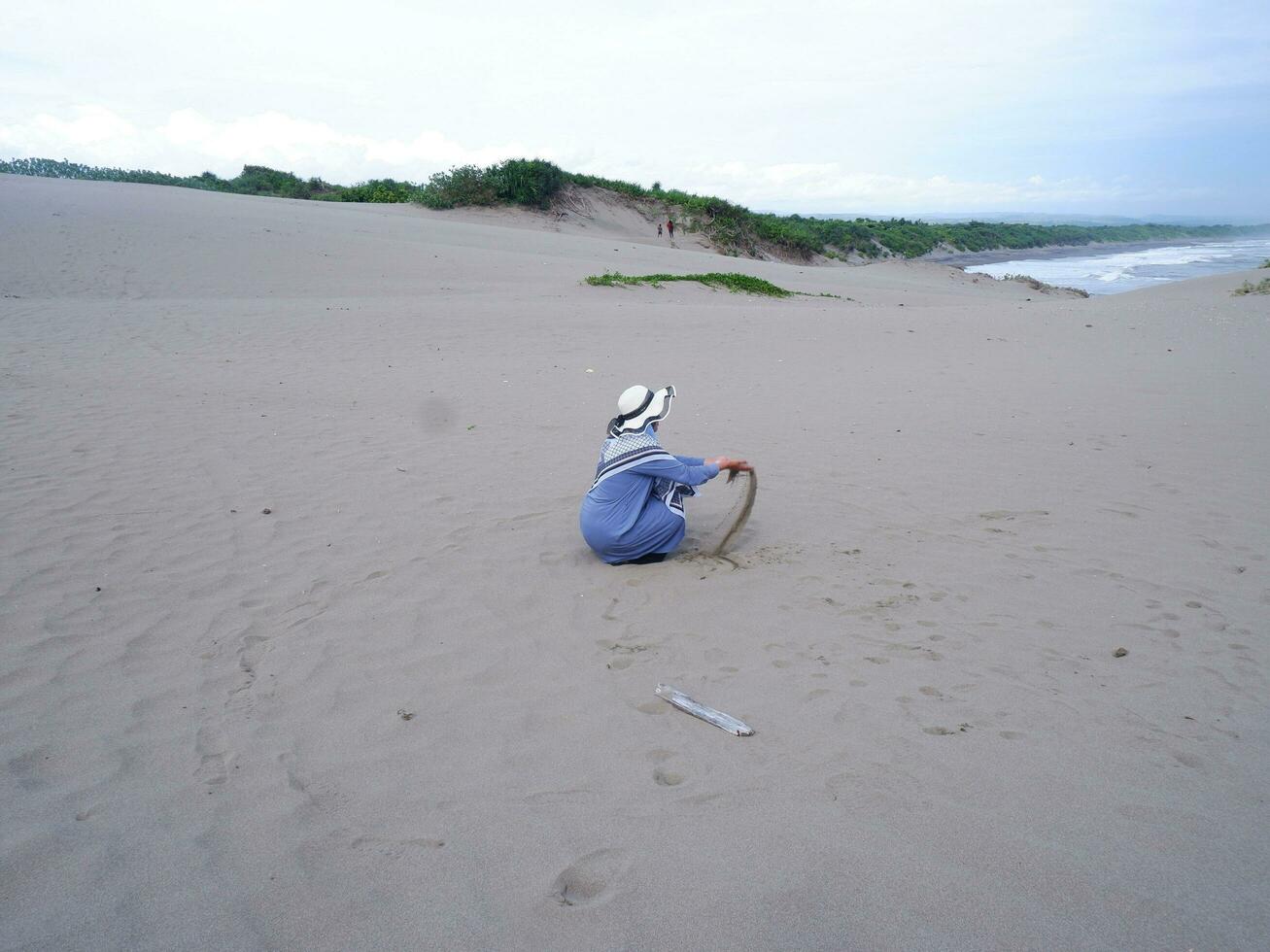 indietro di il donna nel il cappello chi era seduta e giocando spiaggia sabbia, il Visualizza di il sabbia foto