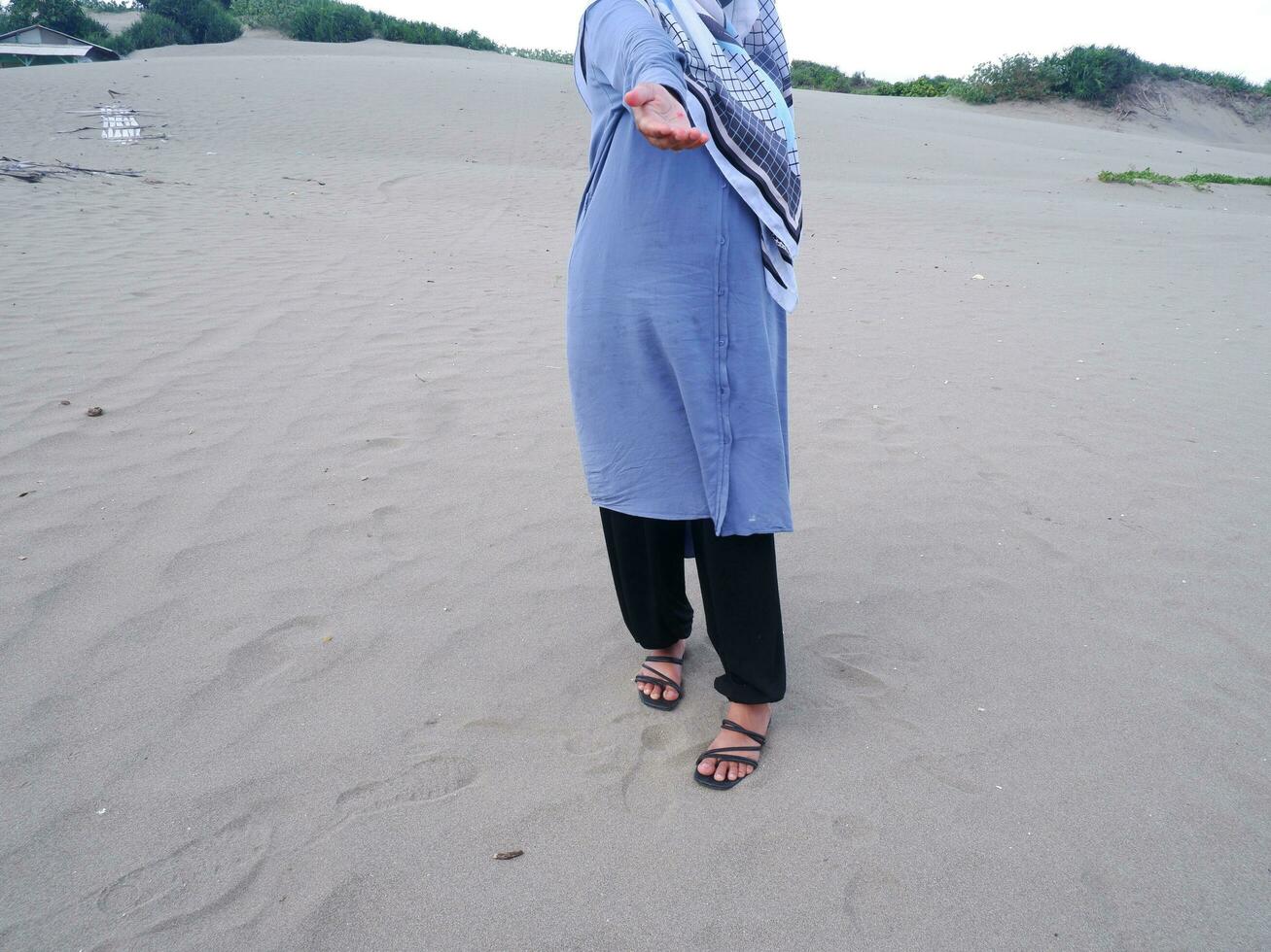 metà il corpo di il donna nel blu si fermò su il spiaggia sabbia e sua mani erano sollevato Aperto per il davanti foto