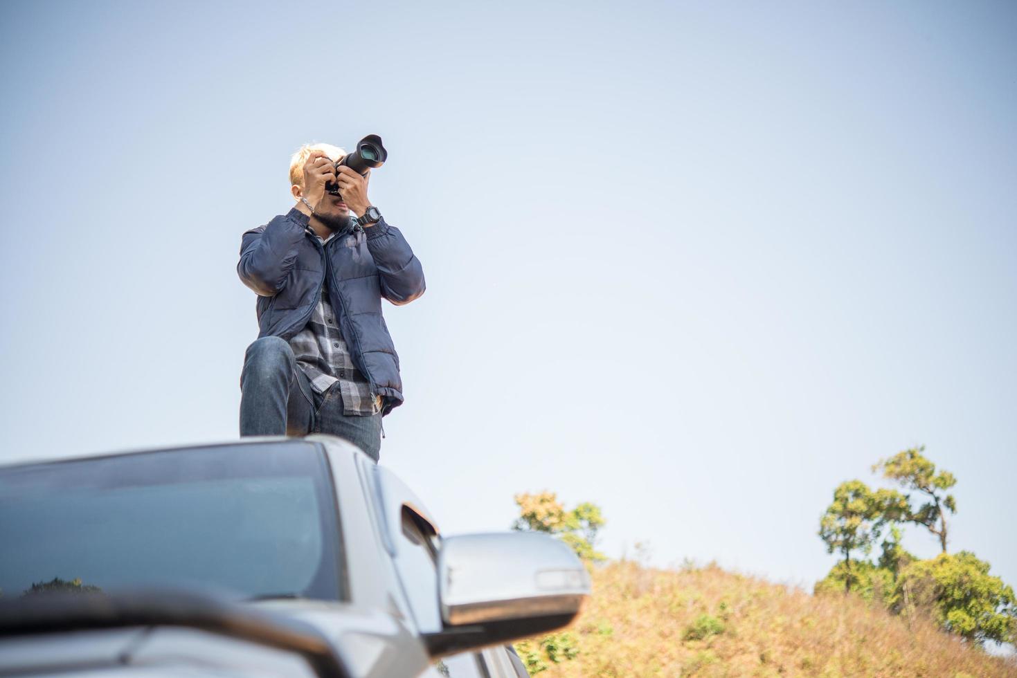 giovane fotografo seduto sul suo camioncino che fotografa una montagna foto
