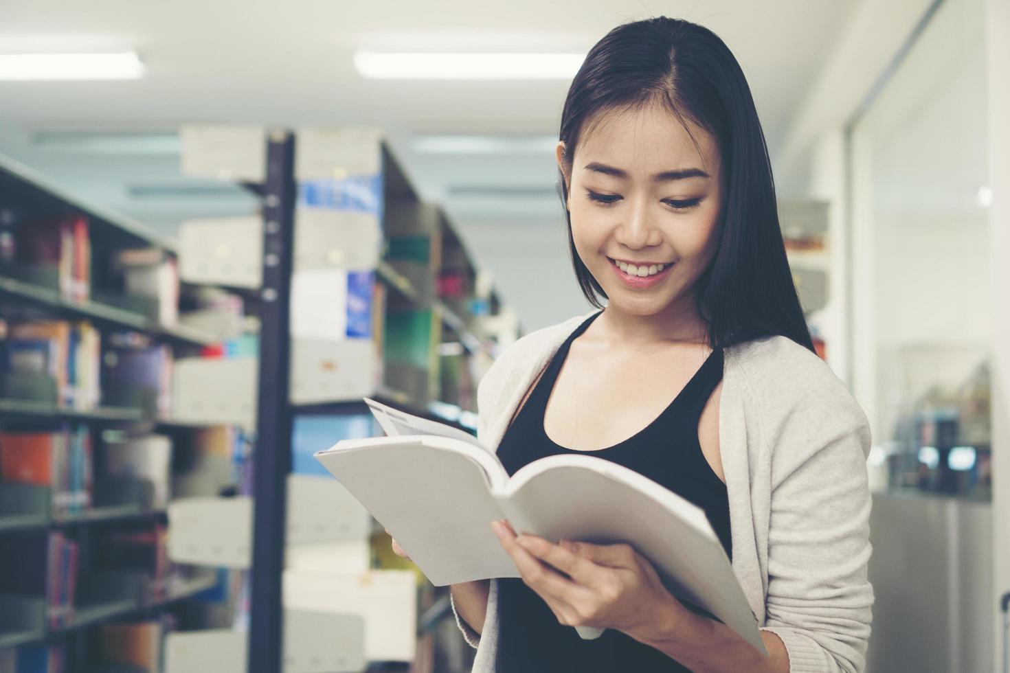 giovane studente asiatico che legge in biblioteca foto