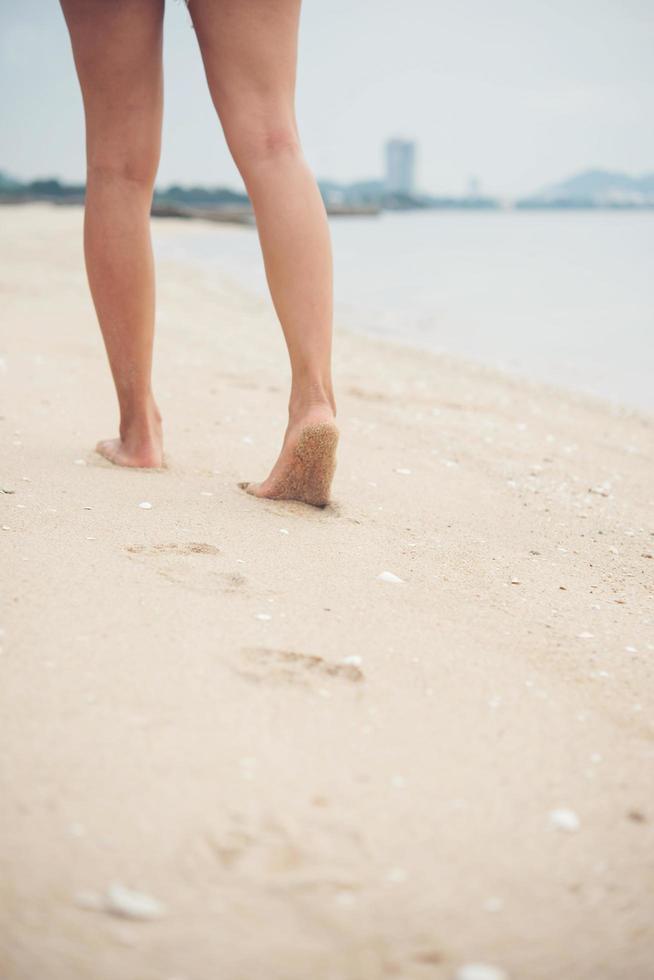 giovane donna che cammina sulla spiaggia di sabbia lasciando impronte nella sabbia foto