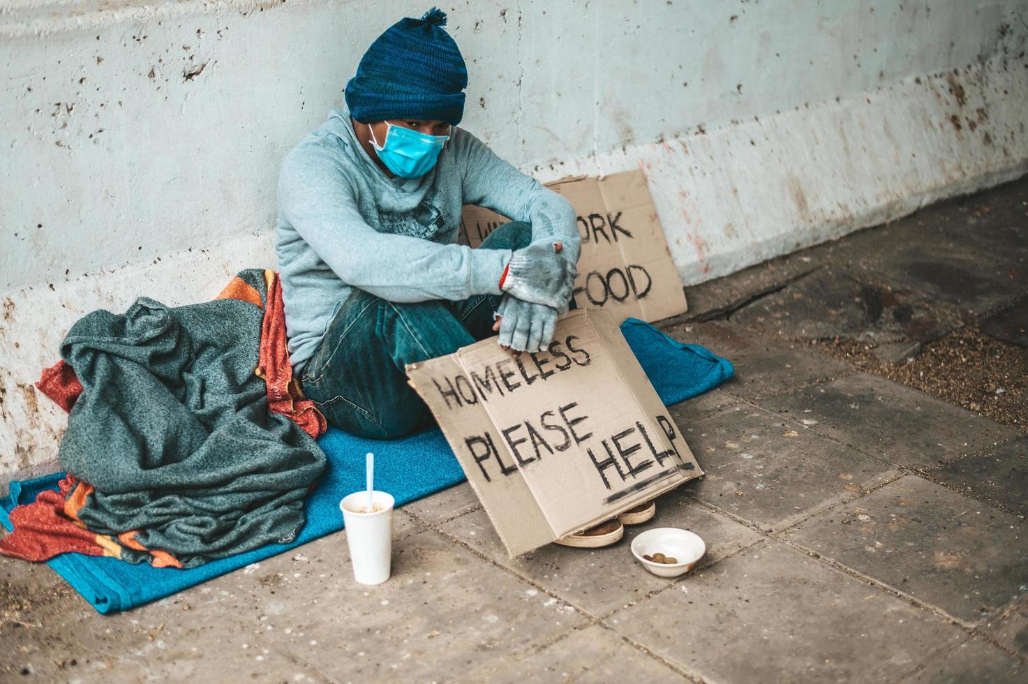 l'uomo si siede accanto alla strada che indossa una maschera medica con un messaggio di senzatetto foto